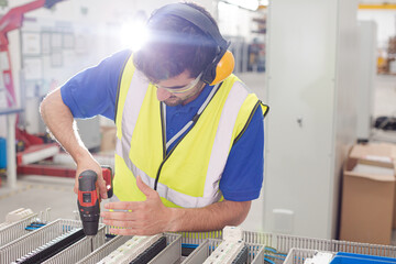Male engineer with power drill assembling equipment in steel factory