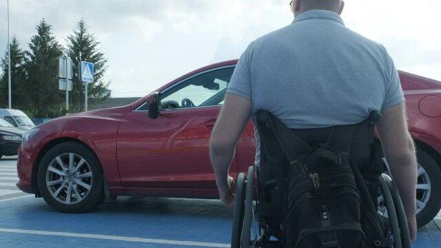 Young handicapped driver getting in red car from wheelchair