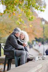 Active senior couple talking, enjoying coffee at autumn park cafe