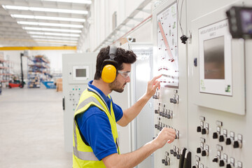 Male worker wearing ear protectors, operating machinery at control panel in factory