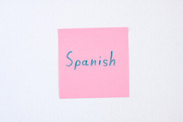 Top view flat lay of the reminder notepaper of pink color with word Spanish on it on white background. Flashcards and language studies concept