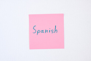 Top view flat lay of the reminder notepaper of pink color with word Spanish on it on white...