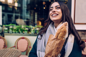 Delighted woman with baguette near bakery on sidewalk