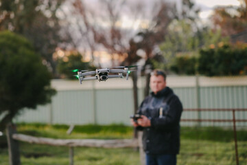 Man flying drone holding remote control on country property at sunset
