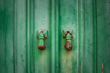 Detail of two rusty door knockers shaped like a woman's hand on vintage green wooden door