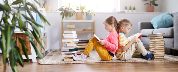 Two children sitting on the floor in the room and reading books - obrazy, fototapety, plakaty