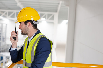 Male supervisor using walkie-talkie on platform in factory