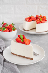 No baked cheesecake with fresh strawberries and mint on top on a white plate on a gray concrete background. Copy space.