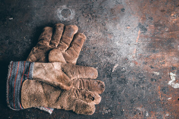 A pair of protection gloves. Old leather gloves on wooden table. Working gloves on wood workbench. A dirty and well-worn pair leather work gloves.