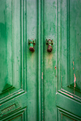 Detail of vintage green wooden door with two rusty door knockers shaped like a woman's hand. Vertical image