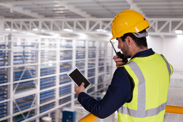 Male supervisor with digital tablet talking, using walkie-talkie on platform in factory