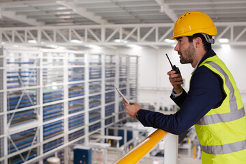 Male supervisor with digital tablet talking, using walkie-talkie on platform in factory
