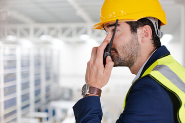 Male supervisor using walkie-talkie on platform in factory