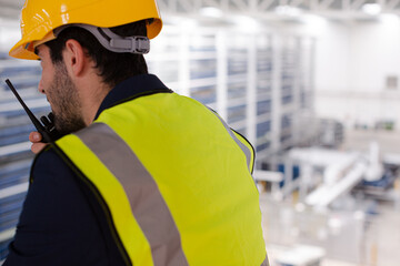 Male supervisor using walkie-talkie on platform in factory