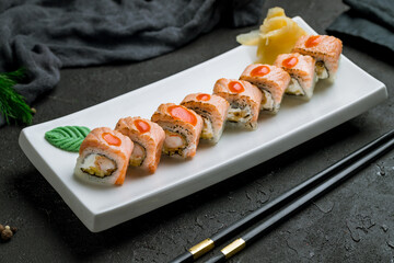 roll with baked salmon and shrimp tempura on white plate on dark stone table