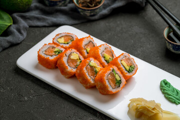 California roll with salmon on white plate on dark stone table