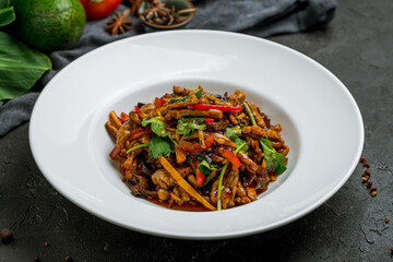 aromatic roast sliced pork with vegetables in hot sauce on white plate on dark stone table