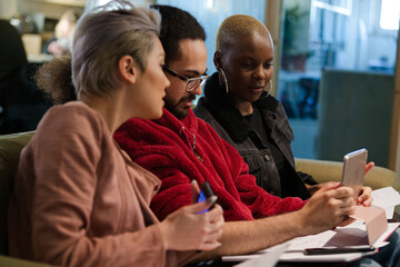 Three colleagues sitting on sofa, discussing paperwork, laughing