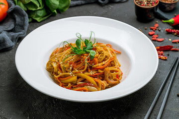 Udon noodles with chicken and vegetables on white plate on black stone table