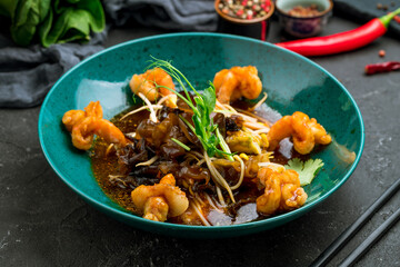 Salad with shrimp and vegetables on blue plate, Chinese cuisine, dark stone table