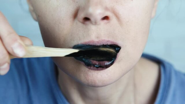 A woman brushes her teeth with activated charcoal. The female is brushing her teeth with an eco brush