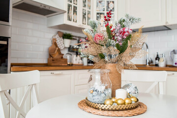 A spruce bouquet with red berries on a white kitchen table. Christmas decorations in the interior. The concept of preparing for the New year holiday.