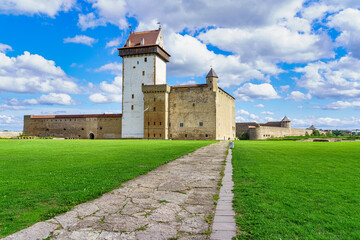Fototapeta na wymiar Narva medieval castle with its stone walls and its access road in the green meadow.