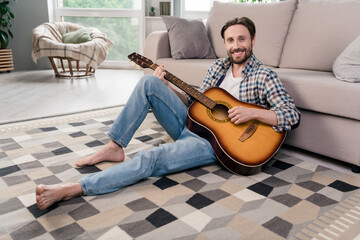 Photo of charming sweet mature guy dressed checkered shirt sitting floor playing guitar indoors apartment room