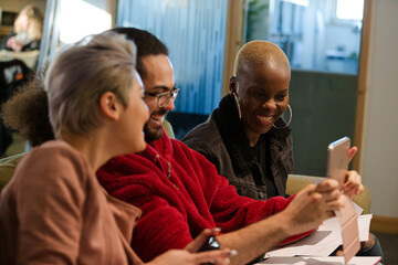 Three colleagues sitting on sofa, discussing paperwork, laughing
