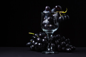 Black grapes on a black background. A bunch of grapes next to an empty glass on a dark background