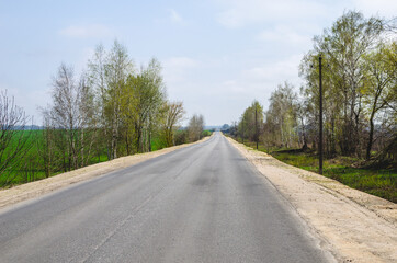 Fototapeta na wymiar Long straight empty motorway surrounded by spring trees receding into the distance in springtime