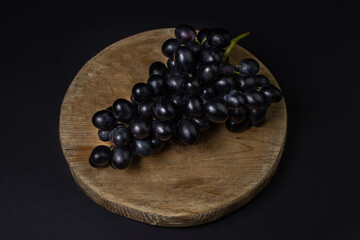 Black grapes on a black background. A bunch of grapes on a wooden plank on a dark background