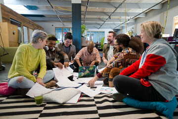 Team sitting on office floor, discussing paperwork