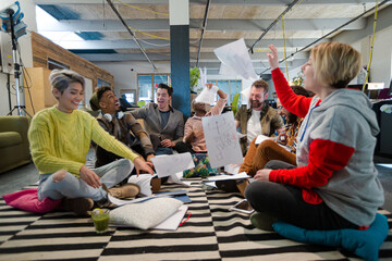 Team sitting on office floor, discussing paperwork