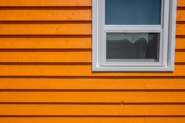 The exterior of a bright orange narrow wooden horizontal clapboard wall of a house with one vinyl window. The trim on the glass panes is white. The outside boards are textured rough pine wood.  - obrazy, fototapety, plakaty
