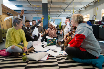 Team sitting on office floor, discussing paperwork