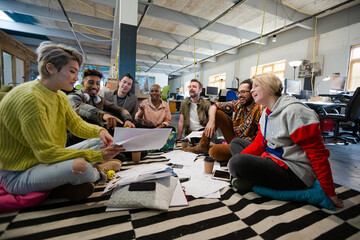 Team sitting on office floor, discussing paperwork