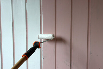 Roller brush painting. Painting wooden walls with white color. Home renovation concept. Worker painting on surface. 