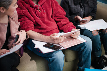 Three friends sitting on sofa, talking and using smartphones