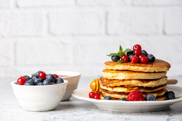 Healthy summer breakfast, homemade classic american pancakes with fresh fruit and honey, morning light gray stone background copy space top view