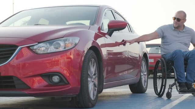 Young handicapped driver getting in red car from wheelchair