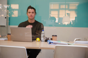 Portrait of young man working at laptop in conference room