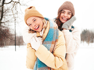 Two young beautiful smiling hipster female in trendy warm clothes and scarfs.Carefree women posing...