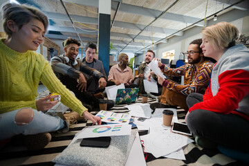 Team sitting on office floor, discussing paperwork