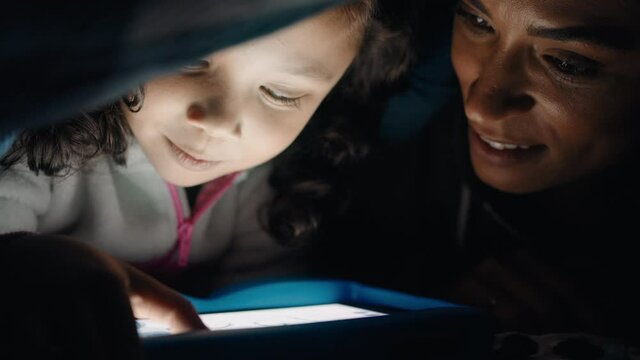 happy mother and daughter using tablet computer under blanket playing games on touchscreen technology relaxing having fun before bedtime 