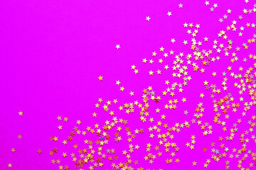 Background of shiny golden small stars on a fuchsia background. Selective focus. Christmas concept. Glitter texture.