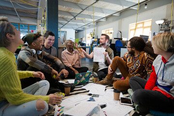 Team sitting on office floor, discussing paperwork