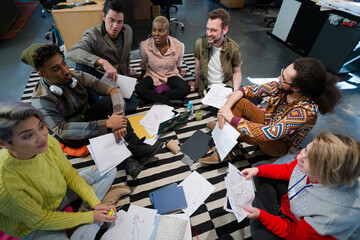 Team sitting on office floor, discussing paperwork