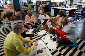 Team sitting on office floor, discussing paperwork