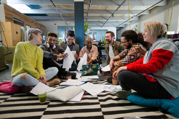 Team sitting on office floor, discussing paperwork